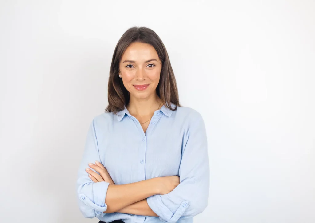 Femme en chemise, de face, croisant les bras avec un sourire.