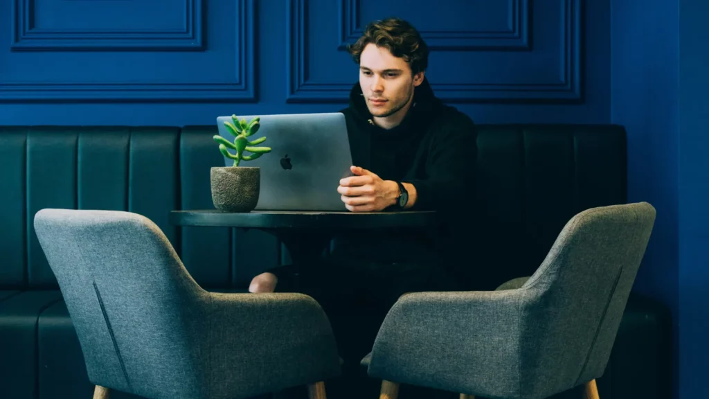 Un homme travaillant sur son ordinateur portable sur une table ronde. Une plante verte se trouve derrière son ordinateur portable.